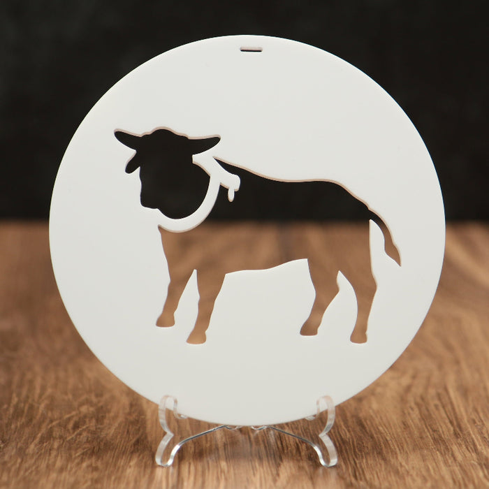 A round white Christmas ornament featuring a bull silhouette cutout, displayed on a clear acrylic stand over a wooden surface against a dark background.
