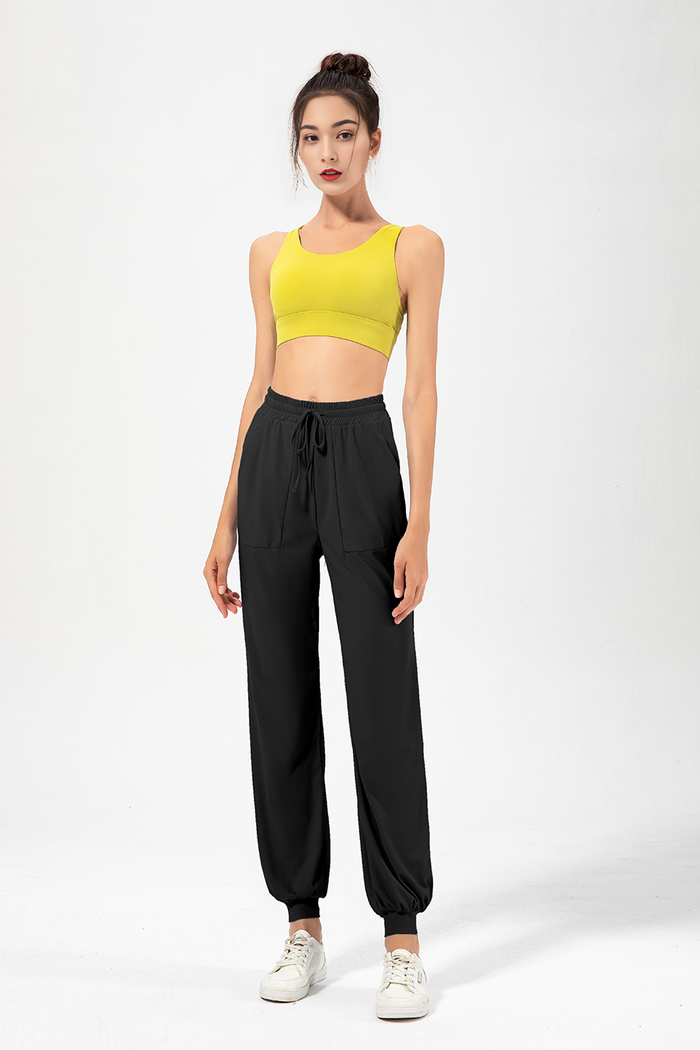 A female model wearing high-rise jogging pants and a yellow sports top.