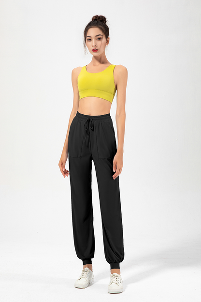 A female model wearing high-rise jogging pants and a yellow sports top.